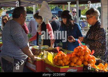 Un vendeur de sexe masculin attend patiemment deux touristes féminins pour choisir une sélection de fruits au marché agricole Victor Harbor en Australie méridionale. Banque D'Images