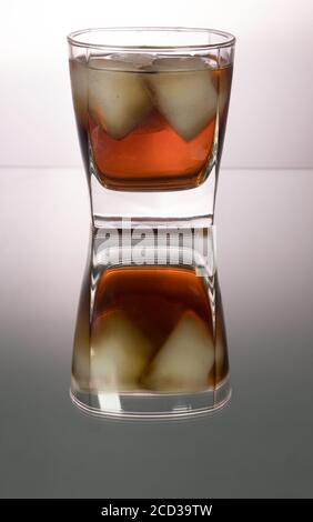 Verre de whisky avec morceaux de glace sur la table miroir. Image verticale avec espace de copie. Banque D'Images