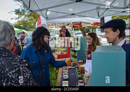 Vue sur le marché local de Victor Harbour en Australie méridionale comme deux frais de touriste pour et recevoir des changements pour les condiments achetés auprès de deux vendeurs. Banque D'Images