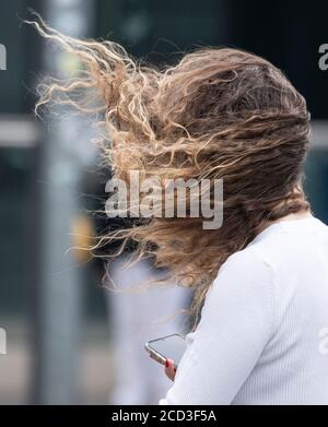 26 août 2020, Hessen, Francfort-sur-le-main : Stormy 'Kirsten' fait sauter les cheveux de cette femme dans son visage alors qu'elle se rend dans le centre-ville. Surtout entre les tours de banque, les rafales de vent gagnent en force supplémentaire. Photo : Boris Roessler/dpa Banque D'Images