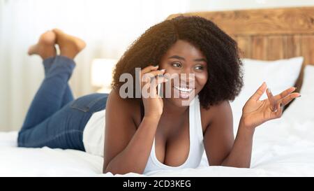 Bonne fille noire couchée sur le lit, parlant sur le téléphone cellulaire Banque D'Images