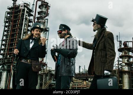 Trois personnes dans le style steampunk discutent de se tenir contre l'industrie arrière-plan Banque D'Images