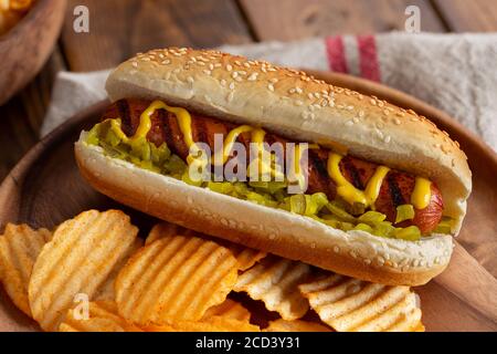 Hot dog grillé à la moutarde et à la sauce au sésame semences de petits pains et de chips de pommes de terre sur une assiette en bois Banque D'Images