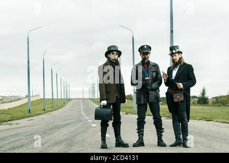 Trois personnes dans le style steampunk posant sur la route Banque D'Images