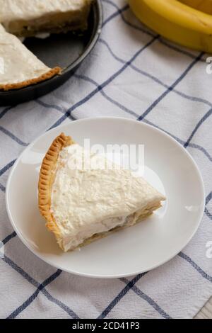 Tranche de tarte à la crème banana maison savoureuse sur fond de bois blanc, vue en angle bas. Gros plan. Banque D'Images