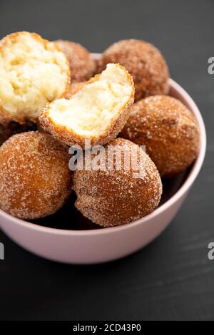 Trous de beignets faits maison dans un bol rose sur fond noir, vue latérale. Banque D'Images