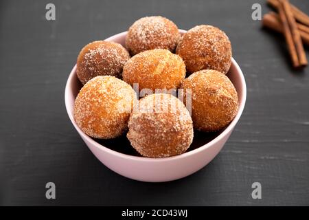 Trous de beignets faits maison dans un bol rose sur une surface noire, vue latérale. Banque D'Images