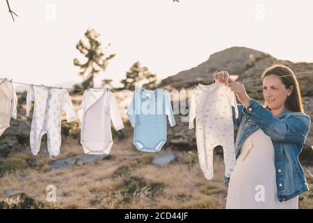 Belle femme enceinte suspendue en plein air vêtements pour enfants. Très bon moment. Banque D'Images