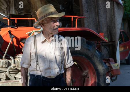 Portrait de très vieux fermier avec chapeau de paille expliquant la vie devant un tracteur rouge. Rétro, gros plan. Banque D'Images