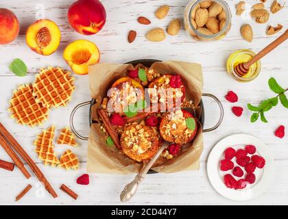 Pêches cuites à la ricotta, aux amandes, à la chapelure de biscuit ou aux gaufres viennoises (belges) et à la cannelle, servies avec du miel, des framboises et de la menthe. Délicieux gou Banque D'Images