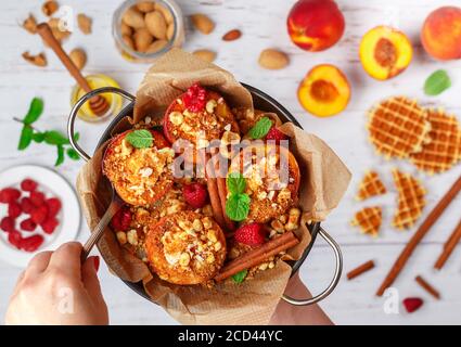 Pêches cuites à la ricotta, aux amandes, à la chapelure de biscuit ou aux gaufres viennoises (belges) et à la cannelle, servies avec du miel, des framboises et de la menthe. Délicieux gou Banque D'Images