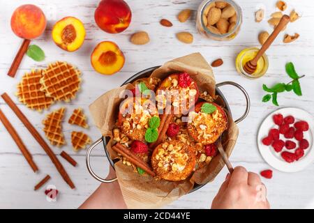 Pêches cuites à la ricotta, aux amandes, à la chapelure de biscuit ou aux gaufres viennoises (belges) et à la cannelle, servies avec du miel, des framboises et de la menthe. Délicieux gou Banque D'Images