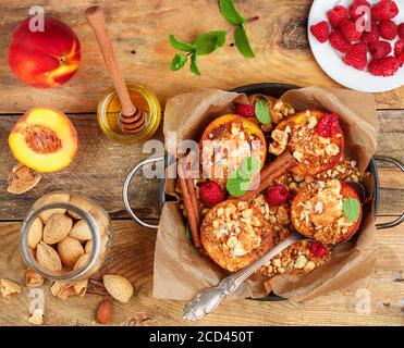 Pêches cuites à la ricotta, aux amandes, à la chapelure de biscuit et à la cannelle, servies avec du miel, des framboises et de la menthe. Délicieux dessert gastronomique. Mise au point sélective, Banque D'Images