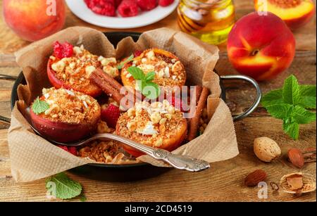 Pêches cuites à la ricotta, aux amandes, à la chapelure de biscuit et à la cannelle, servies avec du miel, des framboises et de la menthe. Délicieux dessert gastronomique. Mise au point sélective Banque D'Images