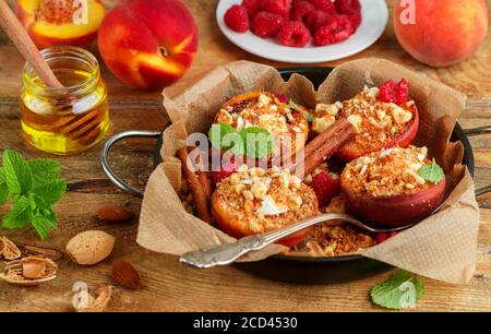 Pêches cuites à la ricotta, aux amandes, à la chapelure de biscuit et à la cannelle, servies avec du miel, des framboises et de la menthe. Délicieux dessert gastronomique. Mise au point sélective Banque D'Images