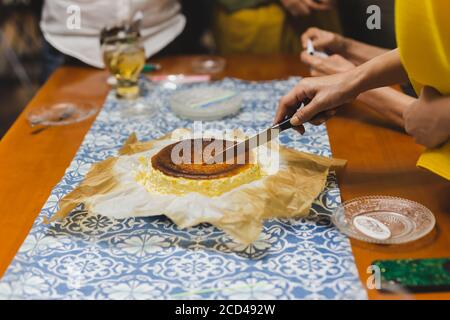 La femme coupe à la main le gâteau d'anniversaire avec la famille. Banque D'Images