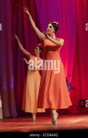 Les jeunes femmes ballerinas dans les robes longues jaune et orange se perforent un spectacle de ballet sur scène au théâtre Banque D'Images