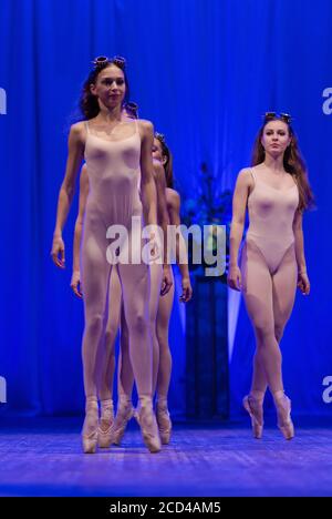 Jeunes femmes ballerines et gymnastes avec de longs cheveux dedans les costumes beiges se réalisent avec un spectacle sur scène dans un théâtre sur fond bleu Banque D'Images