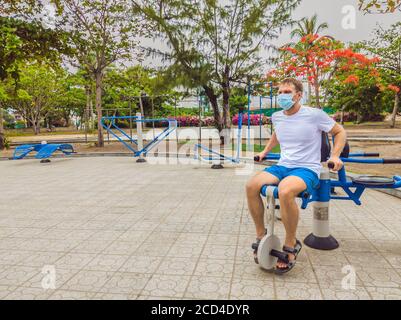 Homme faisant des exercices physiques, des push-up, des exercices de force, se penche dans le parc public extérieur vide de la ville salle de gym en métal portant le masque seul pour Covid19 Banque D'Images