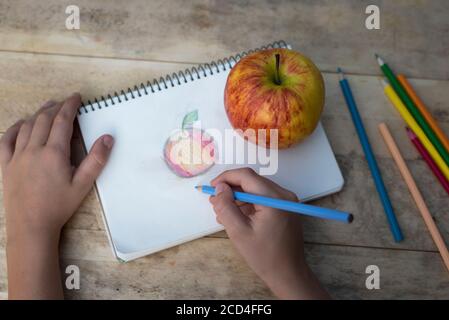 Les mains des enfants dessinent une pomme avec des crayons de couleur. Vue de dessus Banque D'Images