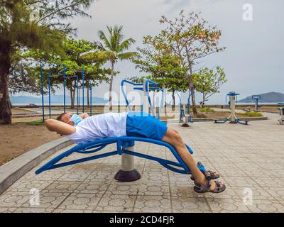 Homme faisant des exercices physiques, des push-up, des exercices de force, se penche dans le parc public extérieur vide de la ville salle de gym en métal portant le masque seul pour Covid19 Banque D'Images