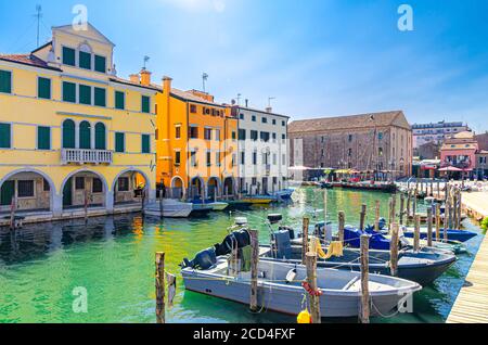 Chioggia paysage urbain avec canal d'eau étroit Vena avec des bateaux multicolores amarrés près de la jetée en bois et des bâtiments colorés, ciel bleu en arrière-plan en été, région de Vénétie, nord de l'Italie Banque D'Images