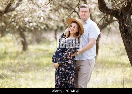 Bonne famille. Femme enceinte et son mari s'embrasent dans le parc de printemps en pleine floraison. Attention sélective Banque D'Images