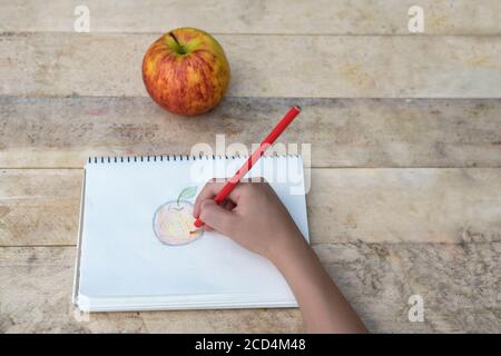 Les mains des enfants dessinent une pomme avec des crayons de couleur. Vue de dessus Banque D'Images