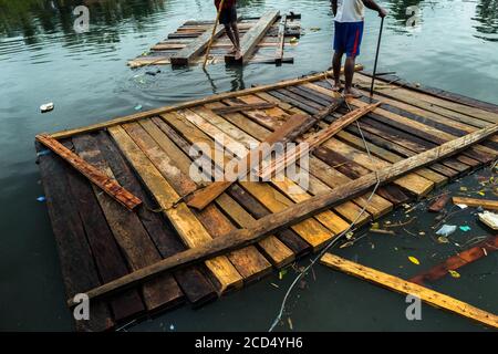 Les transporteurs colombiens équilibrent sur un radeau de bois de sciage brut flottant dans l'eau pendant le transport du bois à Turbo, Colombie. Banque D'Images