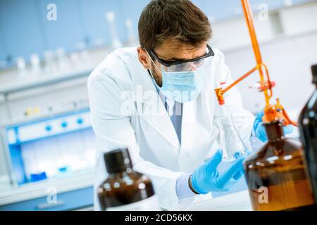 Beau chercheur en vêtements de travail de protection debout dans le laboratoire et flacon d'analyse avec liquide Banque D'Images