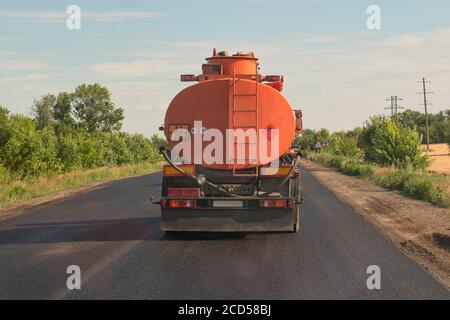 Le camion-citerne orange roule sur une route de campagne contre un ciel bleu. Vue arrière. Banque D'Images