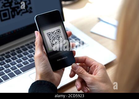 Femme avec un téléphone portable dans sa main scannant un code QR à partir de l'écran de l'ordinateur portable. QR numérisation complète avec l'appareil photo du smartphone. Banque D'Images