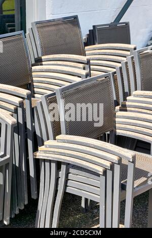 Chaises en métal gris empilées avec accoudoirs en bois sur la terrasse d'un restaurant fermé. Image verticale. Banque D'Images