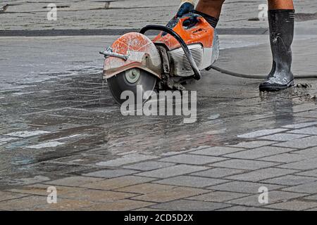 homme travaillant dans des bottes en caoutchouc avec une découpeuse activée la rue Banque D'Images