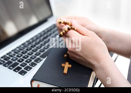 Masse catholique en ligne. Foi et prière. Une femme prie le rosaire. Une femme prie sur un rosaire devant un ordinateur. Banque D'Images