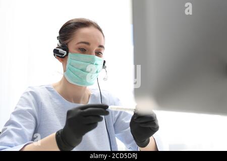 Maladie au travail, température élevée. Une femme dans un masque chirurgical travaille sur l'ordinateur. Travail pendant la peste. h Banque D'Images