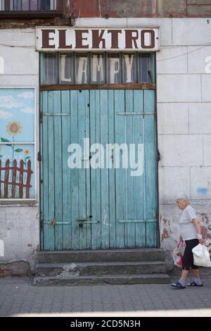 Une vieille dame, une résidente du quartier de Varsovie Praga, avec des sacs de shopping passe devant un magasin d'électricité fermé. La vie quotidienne dans la rue dans le Praga di Banque D'Images