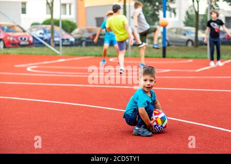 POZNAN, POLOGNE - 24 août 2020 : jeune petit garçon caucasien polonais tenant un ballon de football en cuir avec des drapeaux sur un terrain de sport public. Banque D'Images