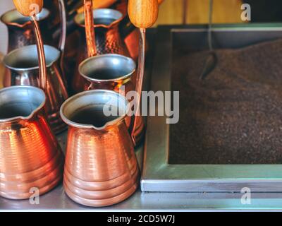 des turcs en métal de couleur bronze brillant se tiennent à côté du sable pour faire café oriental Banque D'Images