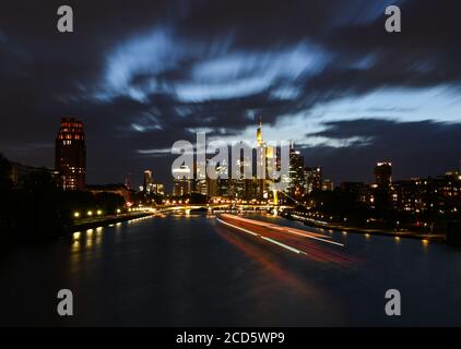 26 août 2020, Hessen, Francfort-sur-le-main : tandis que les nuages sont chassés par des rafales de vent au-dessus de l'horizon illuminé de la ville bancaire, un navire de fête laisse ses traces sur le main. (Prise de vue avec une vitesse d'obturation plus élevée) photo : Arne Dedert/dpa Banque D'Images