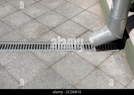 une amélioration de la ville d'ingénierie un déversoir avec une grille de drainage sur un fond d'un trottoir en granit de pierre grise de carreaux carrés, vue latérale c Banque D'Images