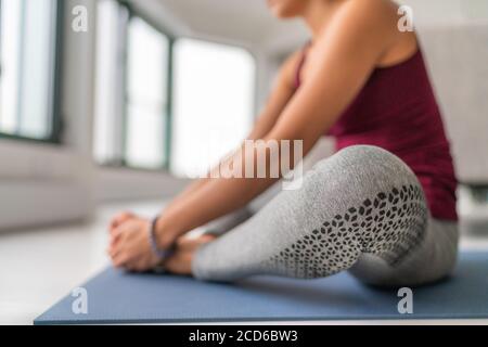 Classe de yoga femme stretching jambes sur tapis d'exercice. Jambe papillon en position assise extensible tenant les semelles des pieds ensemble avec les mains. Gros plan sur les jambes Banque D'Images