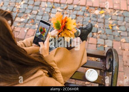 Femme assise au parc de la ville de boire du café de prendre photo de bouquet de feuilles d'érable Banque D'Images