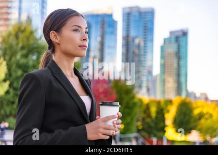Femme d'affaires asiatique qui a fait une pause-café à l'extérieur du bureau pensive et contemplative en regardant à l'extérieur de la ville en arrière-plan. Femme d'affaires Banque D'Images