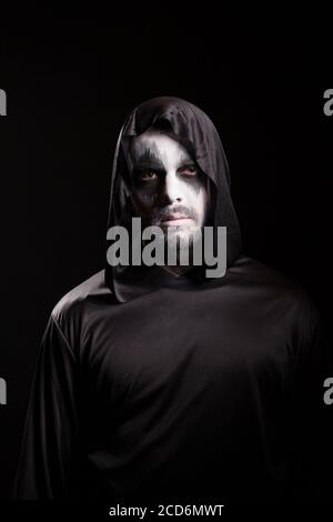 Homme avec un maquillage effrayant pour halloween portant une capuche isolée sur fond noir. Banque D'Images