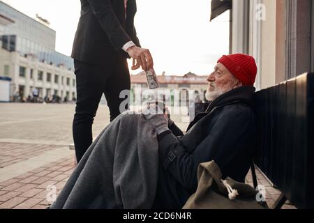 Un homme riche est venu aider un homme sans domicile assis sur le sol. Aide, don d'argent à un homme vagabond dans la rue Banque D'Images