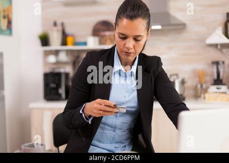 Femme d'affaires effectuant le paiement en ligne par carte de crédit sur un ordinateur portable pendant le petit déjeuner. Acheter en ligne des biens et des vêtements, en utilisant la technologie moderne dans la vie quotidienne, faire des paiements par Internet Banque D'Images