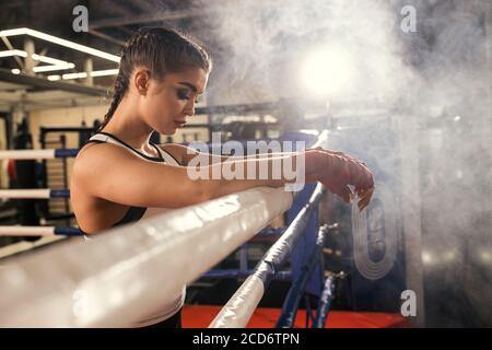 jeune femme caucasienne après espar intense efficace en anneau, femme brune portant des vêtements de sport debout ayant le repos après l'entraînement, boxe Banque D'Images