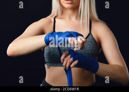 Beau blond caucasien Muay Thai chasseur enveloppant ses mains avec un groupe, se préparant dans le sport d'arène de boxe Banque D'Images