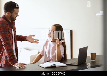 Gai jolie femme et mari gentiment parler dans une chambre confortable et lumineuse, homme impressionnant s'étendant de la paume vers la jeune fille en disant des nouvelles agréables, e Banque D'Images